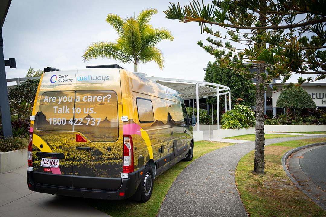 A colourful van parked on a nature strip next to a building and a palm tree