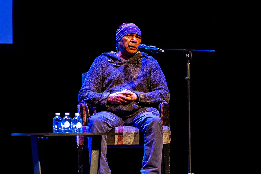 A person sitting on a chair on stage with a microphone.