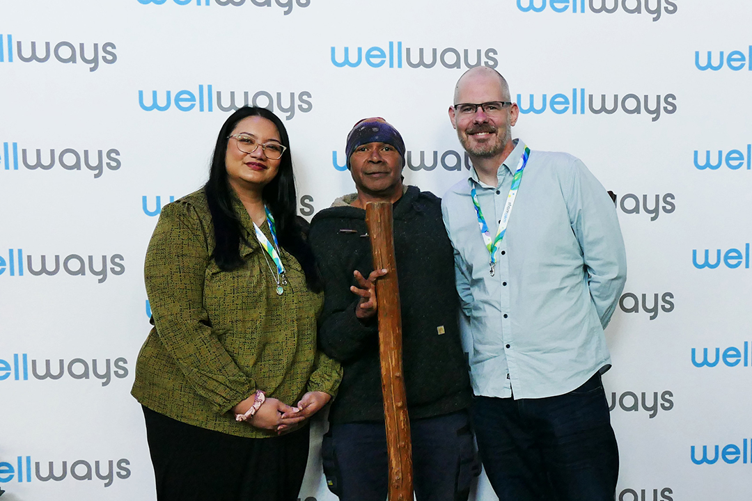 Three people in front of a branded media wall.