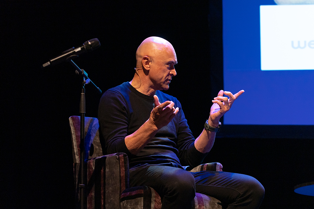 A person sitting on a chair on stage with a microphone.