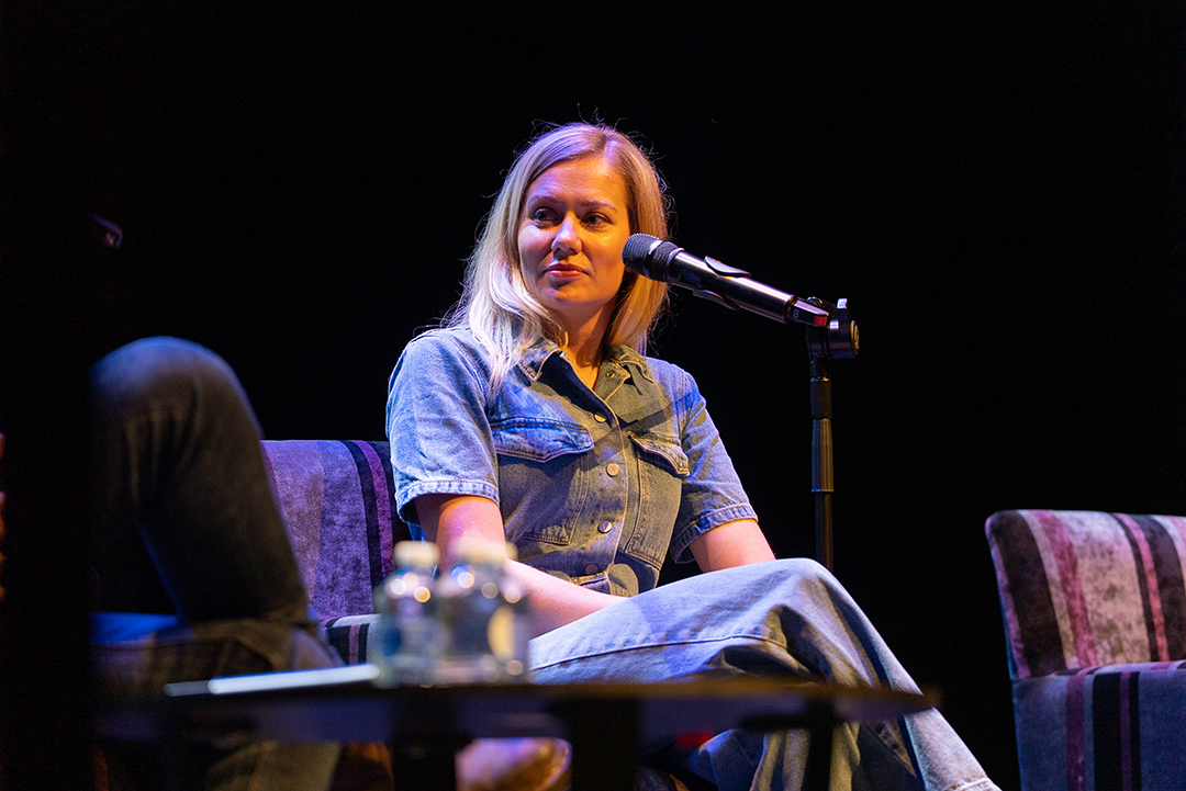 A person sitting on a chair on stage with a microphone.