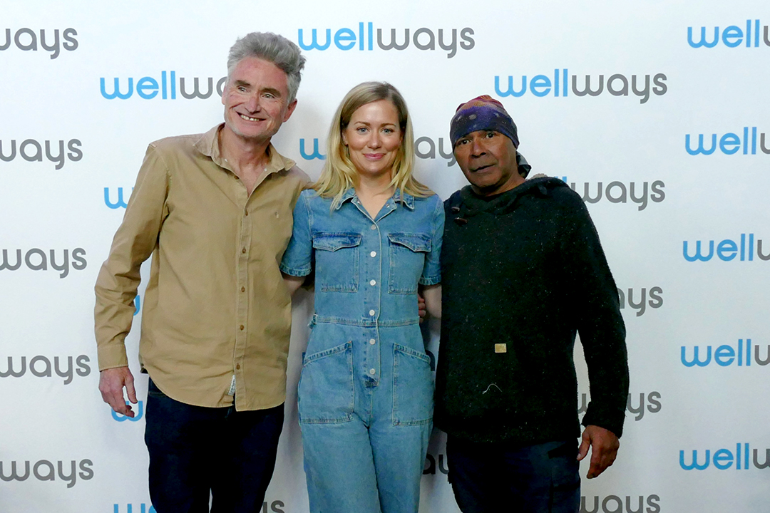 Three people in front of a branded media wall.