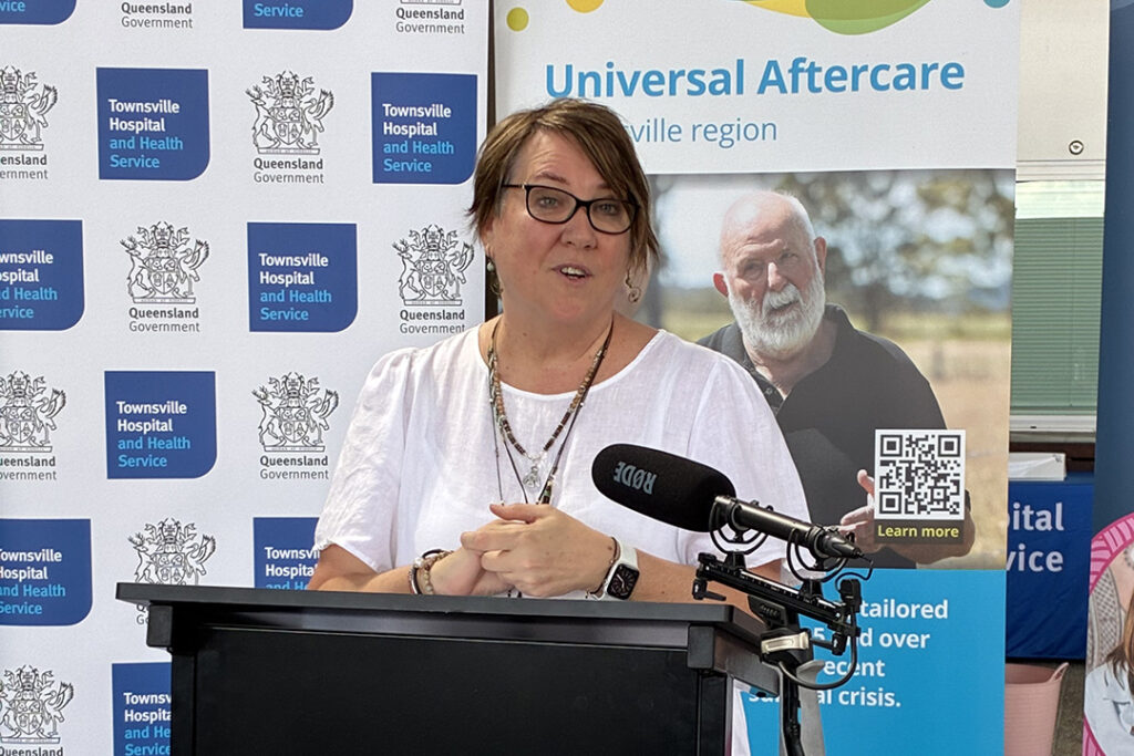 A person in a white shirt standing behind a lecturne in front of various banners.