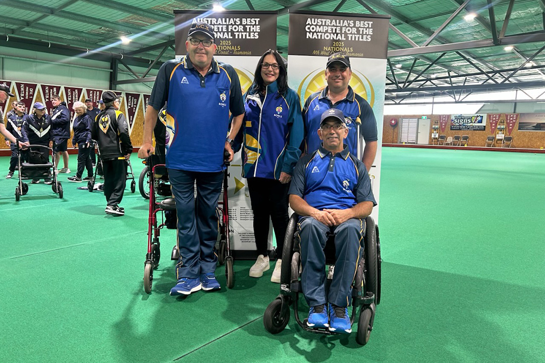 Four people dressed in blue and yellow team clothing at an indoor lawn-bowls event