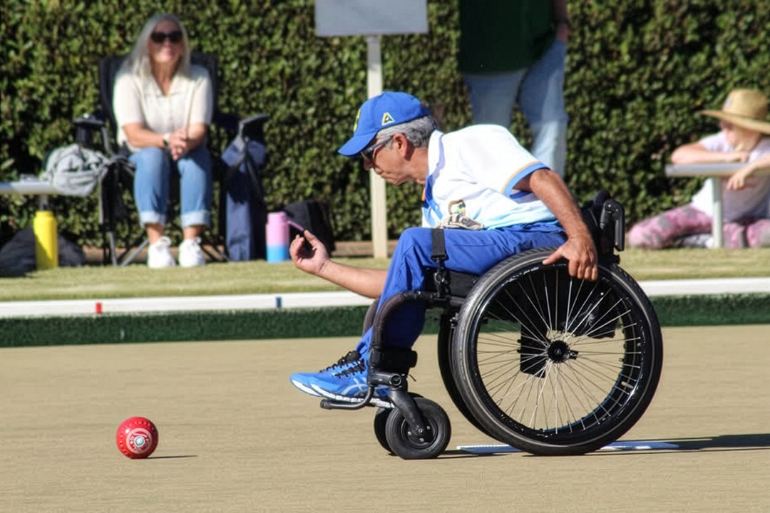 A person in a wheelchair wearing blue and yellow clothes playing lawn bowls