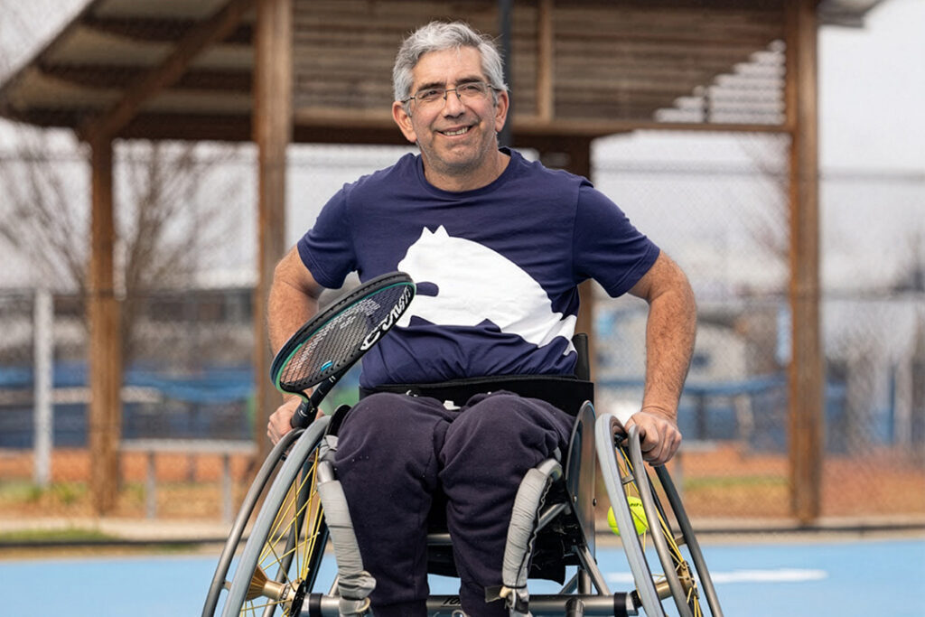 A person in a wheelchair on a tennis court holding a tennis racket