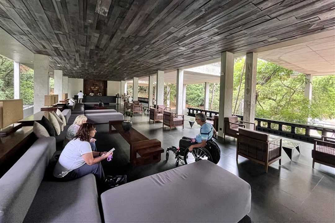 A person in a wheelchair with two other people seated on outdoor furniture under cover