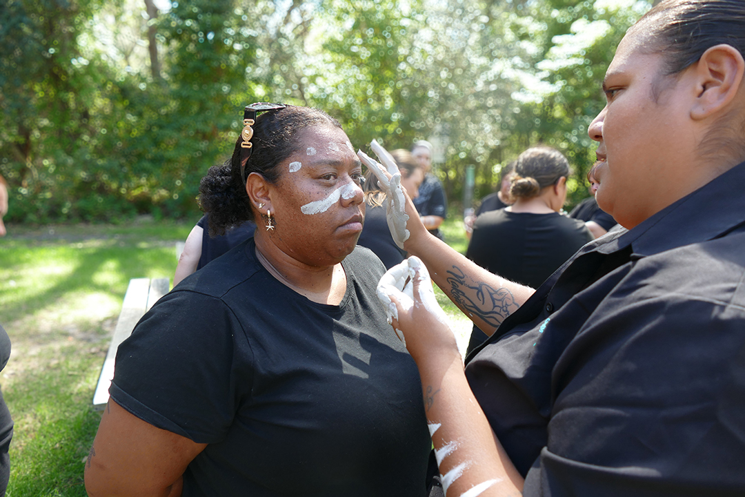 A person applies white ochre paint onto the cheeks of another person. 