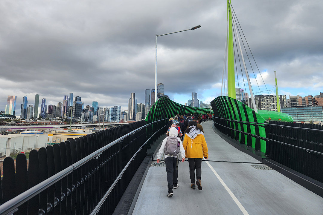 A group of people walking on the Footscray Road Bridge towards Melbourne CBD