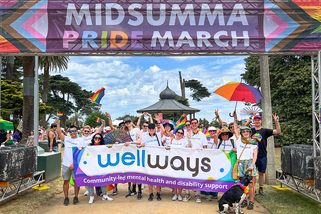 A crowd of people holding a Wellways banner under a large sign. 