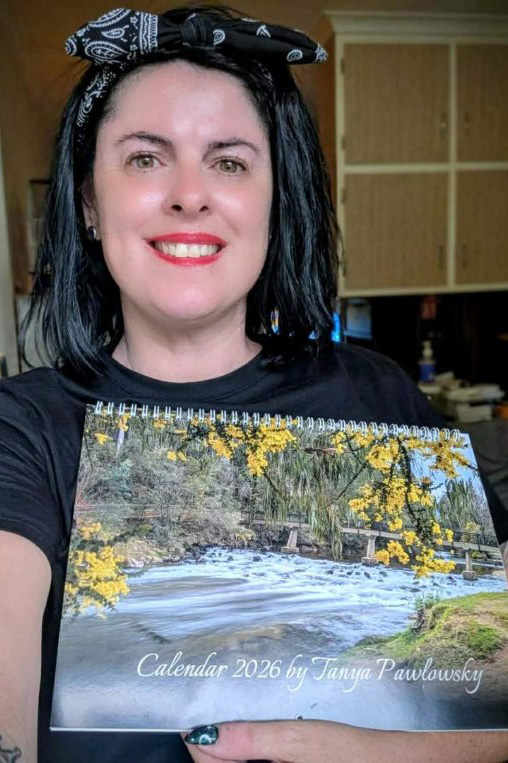 A person with dark hair and red lipstick holding a calendar with a nature scene on the cover