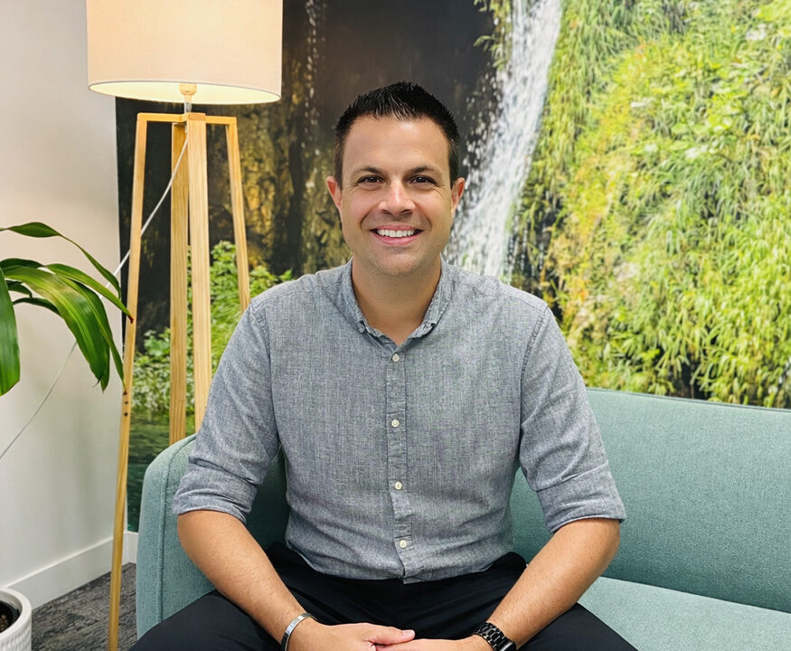 A person in a grey shirt sitting on a lounge in a room with lots of indoor plants