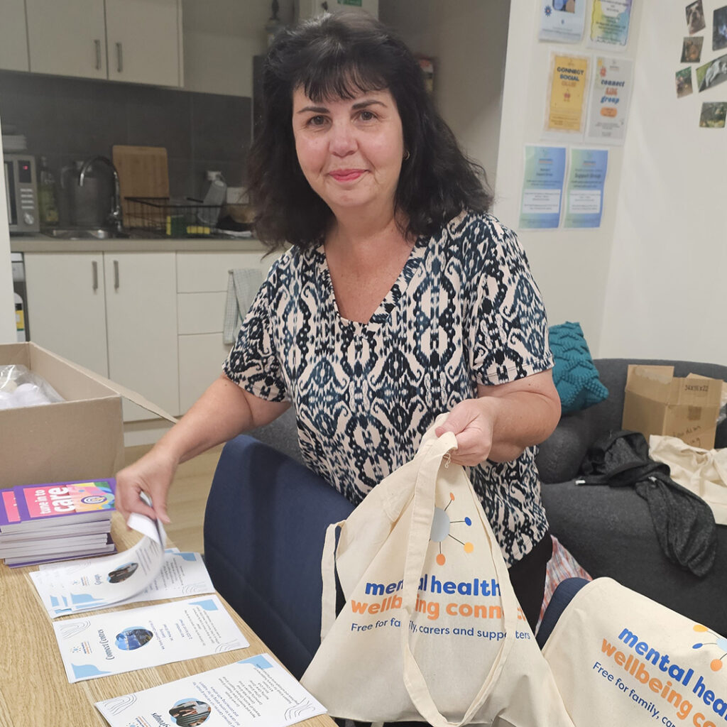 A person with dark hair wearing a pattern shirt is adding pamphlets to branded tote bags