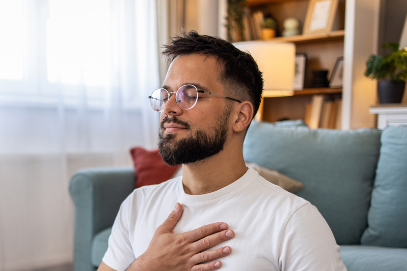 A young person wearing glasses, sitting on the floor meditating in a lounge room