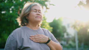 Elderly woman meditating in the park with one hand resting on her chest