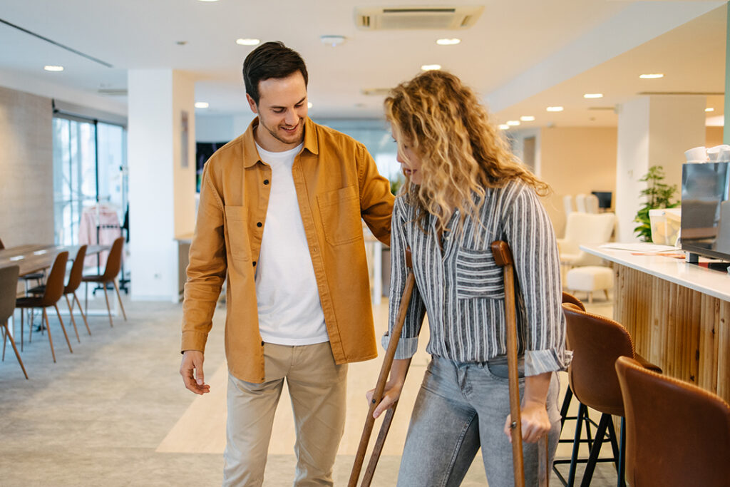A person on crutches is being assisted by another person while moving through a cafe