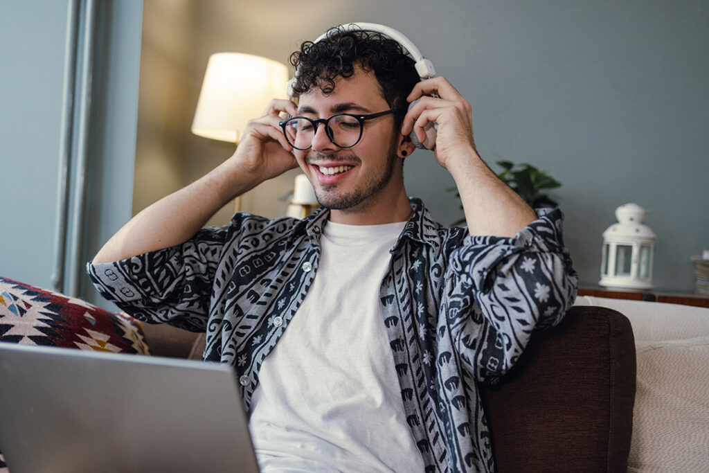 A person sitting on a couch wearing headphones, using a laptop
