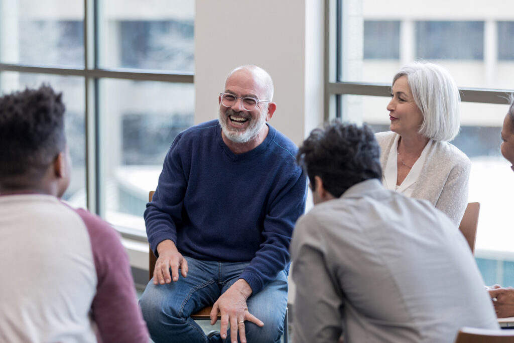 Four people taking part in a group conversation in a room with large open windows.