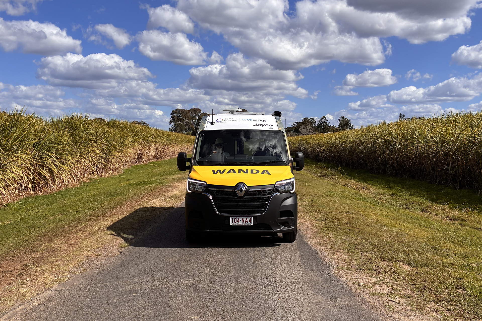 A van with a Wellways Carer Gateway logo and the word Wanda on it's bonnet, driving through a sugar cane field