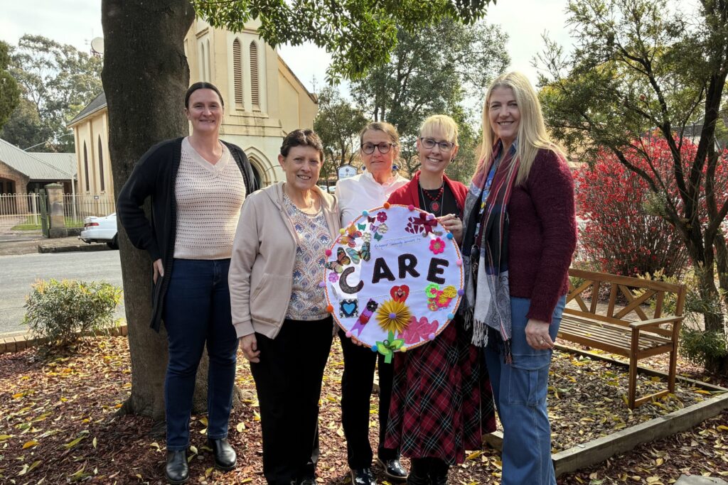 Four people outdoors holding a decorated embroidery hoop