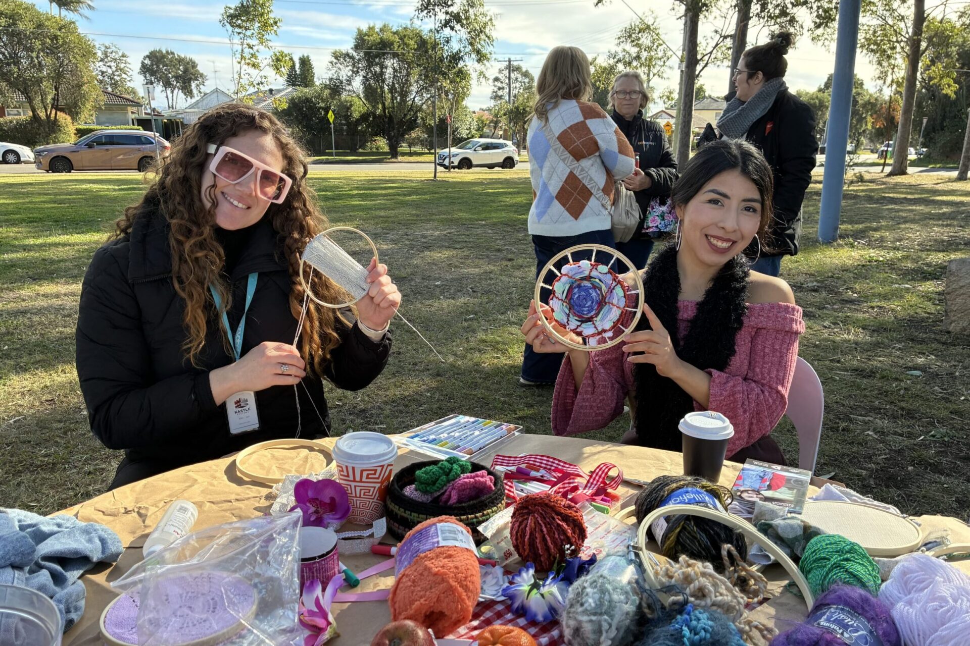 Two people outdoors smiling and holding two decorated embroidery hoops