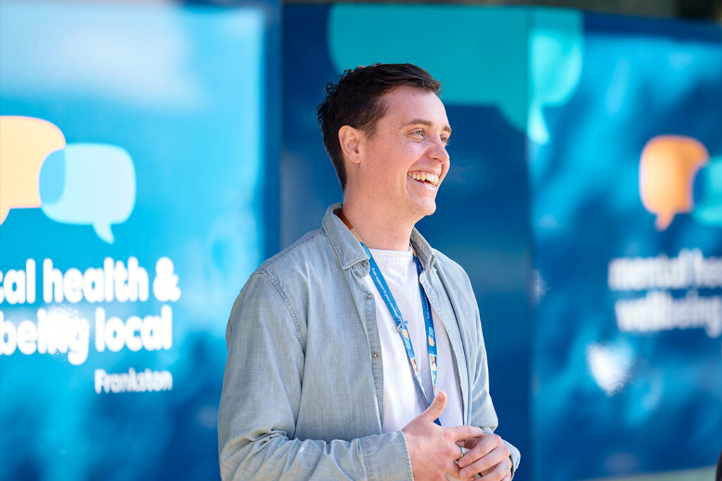 A person smiling in front of a Mental Health and Wellbeing Local building