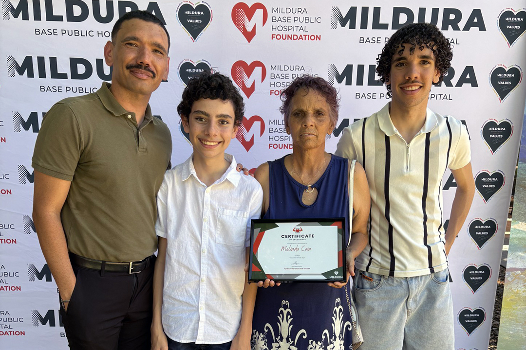 A mother, holding a framed certificate standing with three sons of varying ages, in front of a branded photo wall at an event.