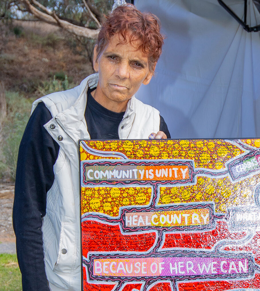 A person outdoors, standing behind a large artwork on a board.